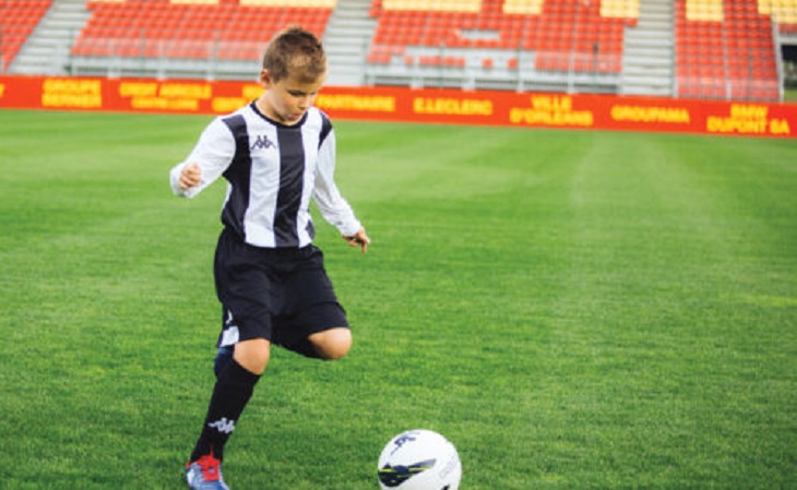 kid wearing kappa jersey on grass and playing football