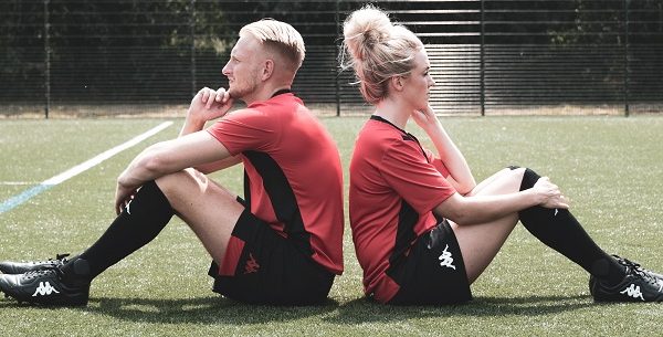 guy and girl sitting on a football field in red jerseys