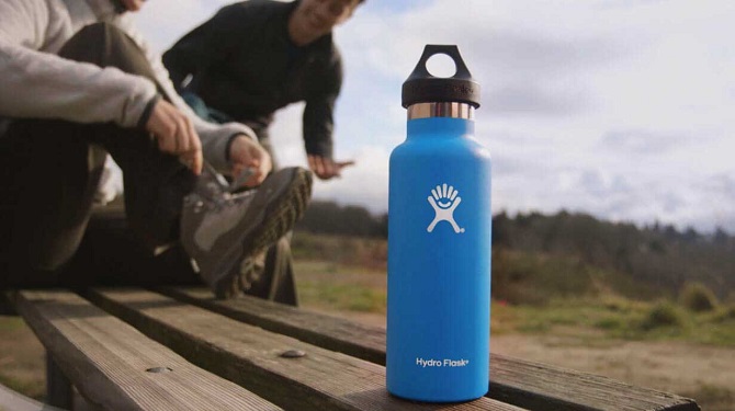 blue hydro flask water bottle on sitting bench and person tying their shoe in the background 