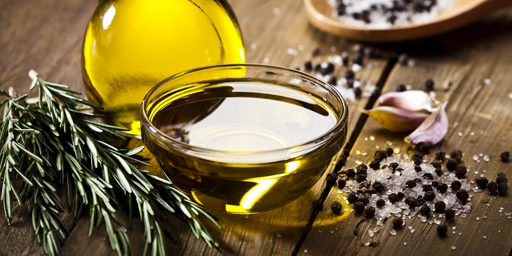 olive oil on a glass bowl on wooden table next to rosemary 