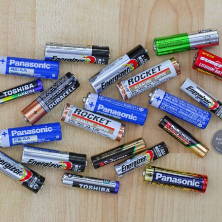 Multiple brands of AA and AAA batteries neatly arranged on light wooden background, illustrating a comparison of battery options available on the market.