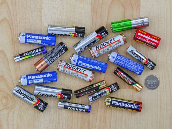 Multiple brands of AA and AAA batteries neatly arranged on light wooden background, illustrating a comparison of battery options available on the market.