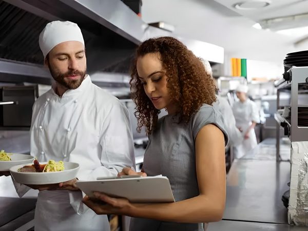 Chef and waitress inspecting dishes in a commercial kitchen.